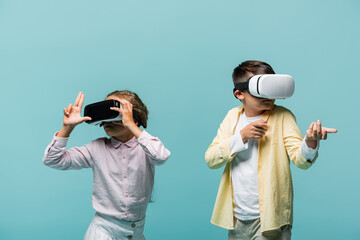 Preteen children in vr headsets playing video game and gesturing isolated on blue.