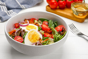 Delicious salad with boiled egg, bacon and vegetables on white wooden table, closeup