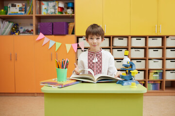 Portrait of ten year old schoolboy wearing embroidered ukrainian vyshyvanka and sitting at the classroom desk with a book