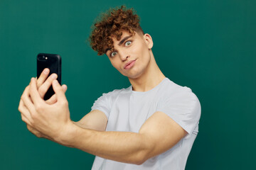 a joyful, handsome man takes a selfie on his smartphone holding it with both hands and smiling broadly. Horizontal studio photo on a green background