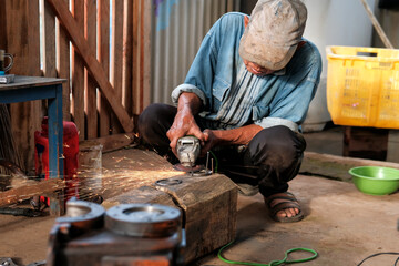 Manual worker using grinder to cut metallic detail in the workshop