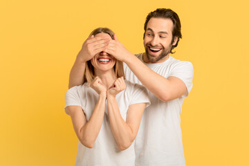 Cheerful glad millennial caucasian guy in white t-shirt closes eyes to woman for surprise