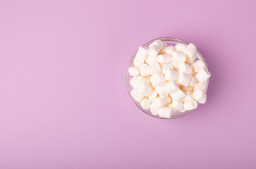 Marshmallows on a lilac background in a glass bowl. White marshmallow flat lay. Sweets and snacks for a snack. Chewing candies close-up. Copy space. Place for text. Winter food concept.