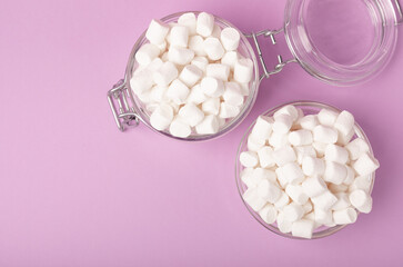 Fototapeta na wymiar Marshmallows in a glass bowl and a jar on a lilac background.Sweets and snacks for a snack.Chewy candy close-up.Copy space.Place for text.