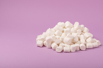 Loose marshmallows on a lilac background. White marshmallow flat lay. Sweets and snacks for a snack. Chewing candies close-up. Copy space. Place for text. Winter food concept.