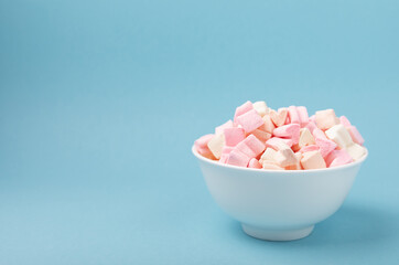 Marshmallows in plates on a blue background.Close-up strawberry flavored chewy candy.Snacks and snacks for parties.Spice for coffee and cocoa.Winter food concept.Place for text.