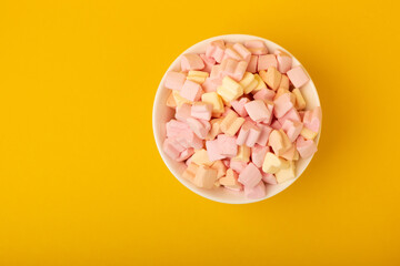 Marshmallows in plates on a yellow background.Closeup strawberry flavored chewy candy.Snacks and snacks for parties.Spice for coffee and cocoa.Winter food concept.Place for text.