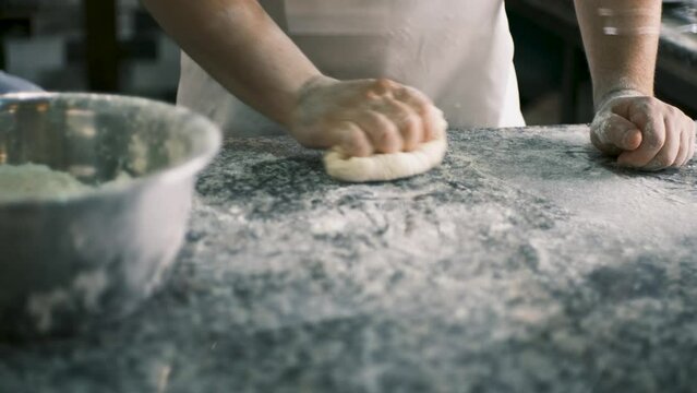 A chef kneads dough from pizza flour with his hands and forms a cake. View from behind the glass. 