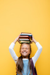 Happy schoolgirl holding books on head isolated on yellow.