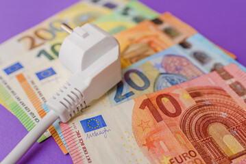Electric plug,euro paper money banknotes.Purple indoors background. Increasing of electricity cost...