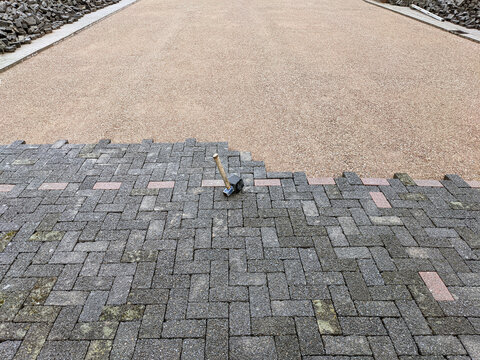 Konzept Baustelle und Sanierung Pflasterung: Draufsicht auf eine Baustelle mit einem halb fertig gepflasterten Grundst&uuml;ck und einem Gummihammer im Vordergrund &ndash; viel Copy Space, Textfreiraum