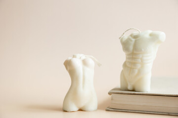 Close up of two handmade candles from soy wax in shape man torso and woman body isolated on pastel beige background.