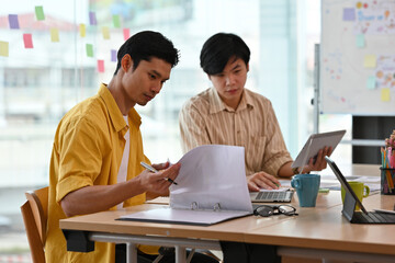 Fototapeta premium A portrait of handsome Asian businessmen working together on a laptop and having a discussion on work in an office, for business and people concept.