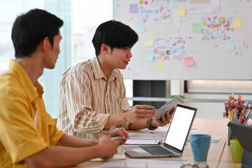 Obraz premium A portrait of handsome Asian businessmen working together on a laptop with a white blank screen and having a discussion on work in an office, for business and people concept.