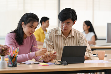 A portrait of a businesswoman and a businessman sitting together working on a laptop and notes, for business and finance concept.