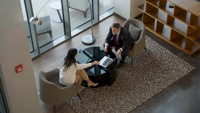 Mature businessman and middle-aged woman having an informal meeting in a lobby, discuss project, have business conversation