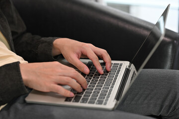 Close up of a man sitting on a sofa and working on a laptop. For business, technology and home concept.