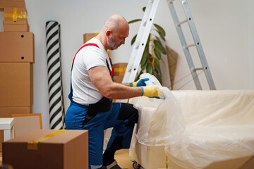 Man mover in uniiform packing sofa for relocation