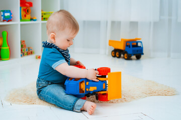 cute baby is sitting on the floor of the house, playing with colorful educational toys