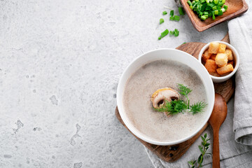 Cream soup with champignons and dill in a white bowl on the table with croutons, top view and copy space