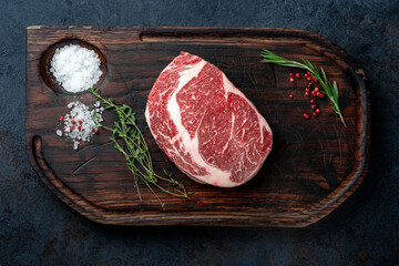 One Raw rib eye steak on a wooden Board on a table prepared for the grill with spices and herbs. Rustic style