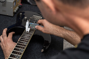 Latin American luthier calibrates the strings of an electric guitar with a digital vernier....