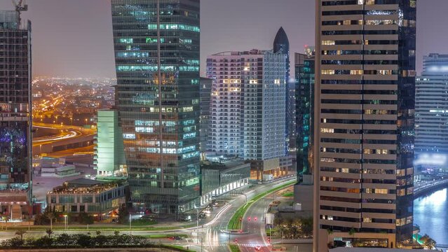 Cityscape of skyscrapers in Dubai Business Bay with water canal aerial night timelapse. Modern skyline with illuminated towers and traffic on intersection. A center of international business
