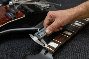Latin American luthier measures the thickness of an electric bass capo with a digital vernier. Unrecognizable. Bass concept, calibration, instrument. - obrazy, fototapety, plakaty