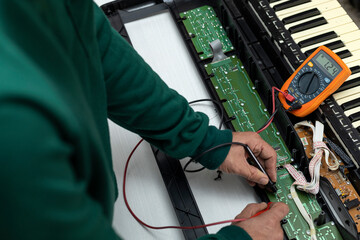 Hands of Latin American electronic technician with a multimeter makes current and resistance measurements to an electronic board of an electric piano in a service center. Repair concept, piano, electr