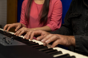 Latin American teacher plays the piano keyboard with her student with four hands. Concept of music...