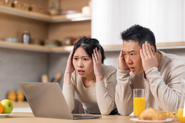 Shocked asian couple looking at laptop screen