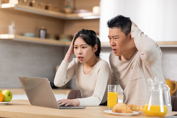 Emotional chinese spouses watching news online at kitchen, copy space