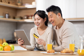 Cute asian couple shopping from home while having breakfast
