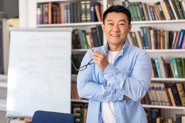 Happy Asian Male Teacher Posing Holding Eyewear Standing In Classroom