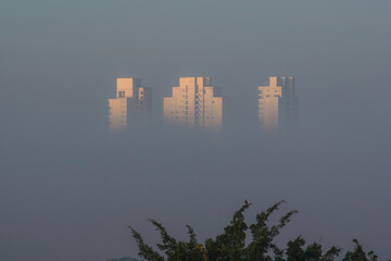 Three towers of a residential complex around the strong fog of a winter morning, showing only the tops of the buildings.