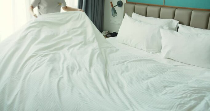 Youngs hard-working females housekeeper in uniform getting luxury hotel room ready by changing white linens while making bed