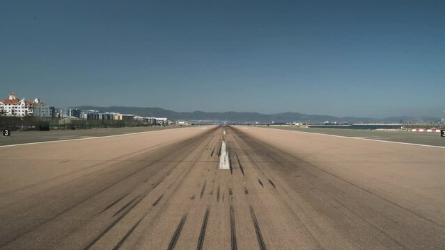 Empty runway with tire marks at Gibraltar airport, cloudless sky above.