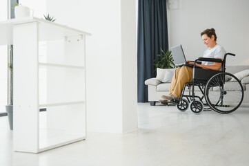 Fototapeta premium Middle age woman using laptop sitting on wheelchair at home