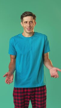 Puzzled man. Unexpected situation. Refusal gesture. What is it. Clueless emotion. Surprised smiling guy shrugging looking around isolated on green vertical.
