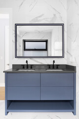 Obraz premium A luxurious bathroom with marble tile covered walls, a blue vanity cabinet, dark grey vanity, and a mirror with a light on the frame.