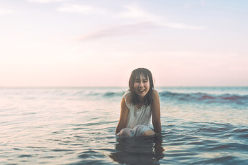 Portrait of asian woman at the beach sitting in the sea waves sunlight background.