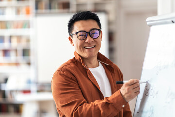 Positive Asian Teacher Man Smiling Writing On Whiteboard In Classroom