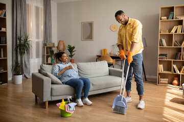African Husband Cleaning House While Wife Using Cellphone At Home