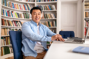 Happy Korean Male Teacher Near Laptop Posing Sitting In Library