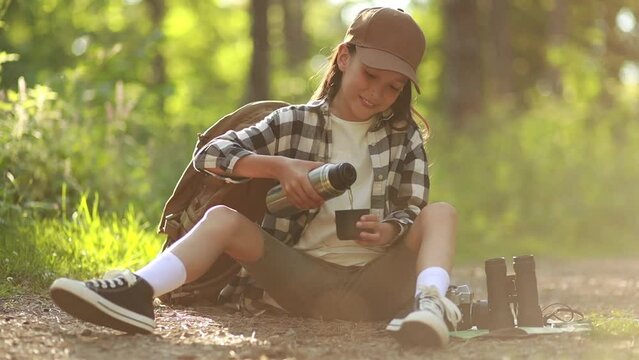 Girl scout sitting and drinking hot tea from thermos in the woods