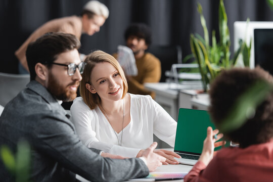 Woman Smiling Near Multiethnic Colleagues And Laptop With Green Screen In Ad Agency.