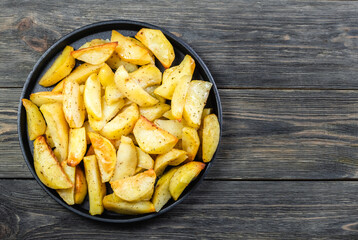 Baked potato wedges in cast iron skillet on wooden background. Top view, copy space, flat lay.