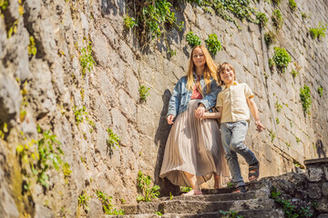 Mom and son tourists enjoying Colorful street in Old town of Perast on a sunny day, Montenegro. Travel to Montenegro concept. Scenic panorama view of the historic town of Perast at famous Bay of Kotor