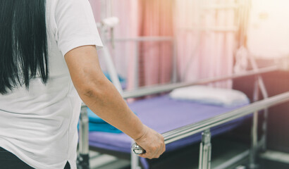 Close up older woman patient walking on parallel bars in rehab room on the background in hospital,...