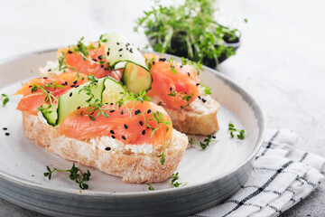 Sandwiches. Salmon toast with cream cheese, cucumber, black sesame and microgreens on gray concrete table background. Seafood. Healthy food. Top view.